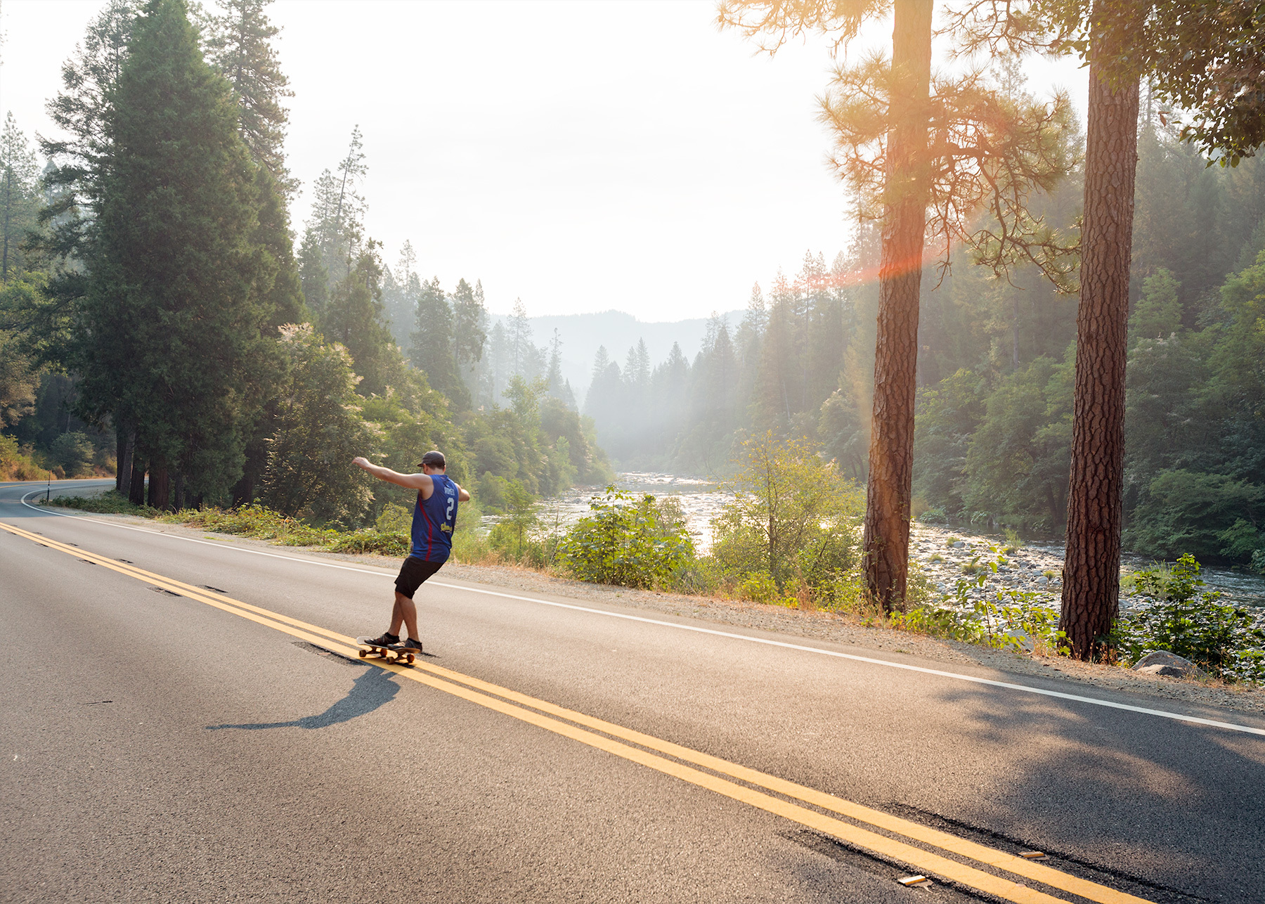 Matt skateboarding down a highway with trees and a river in the background in California